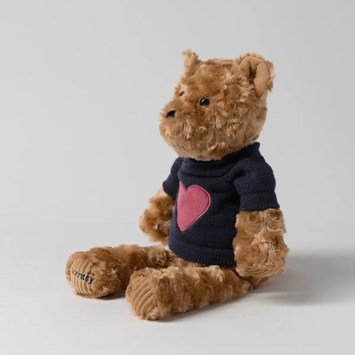 Tan plush bear with black button eyes wearing a dark navy sweater with a pink heart design