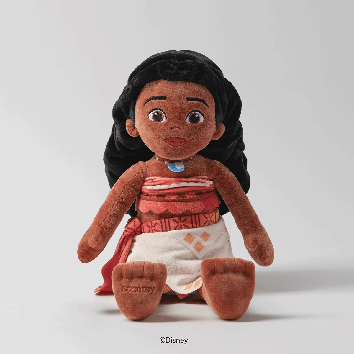 Soft plush toy of Moana with black long hair, brown skin, white and coral dress with blue necklace, embroidered Scentsy logo on feet