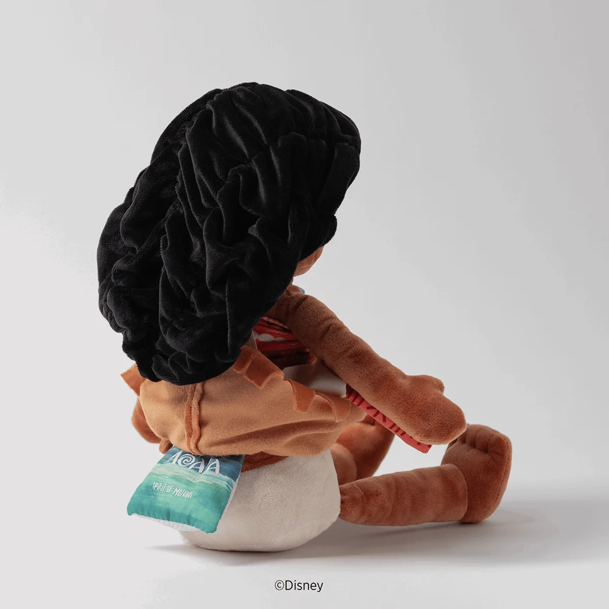 Soft plush Moana character with black wavy hair, brown arms, tan torso, and white belly, seated with Scentsy product label visible