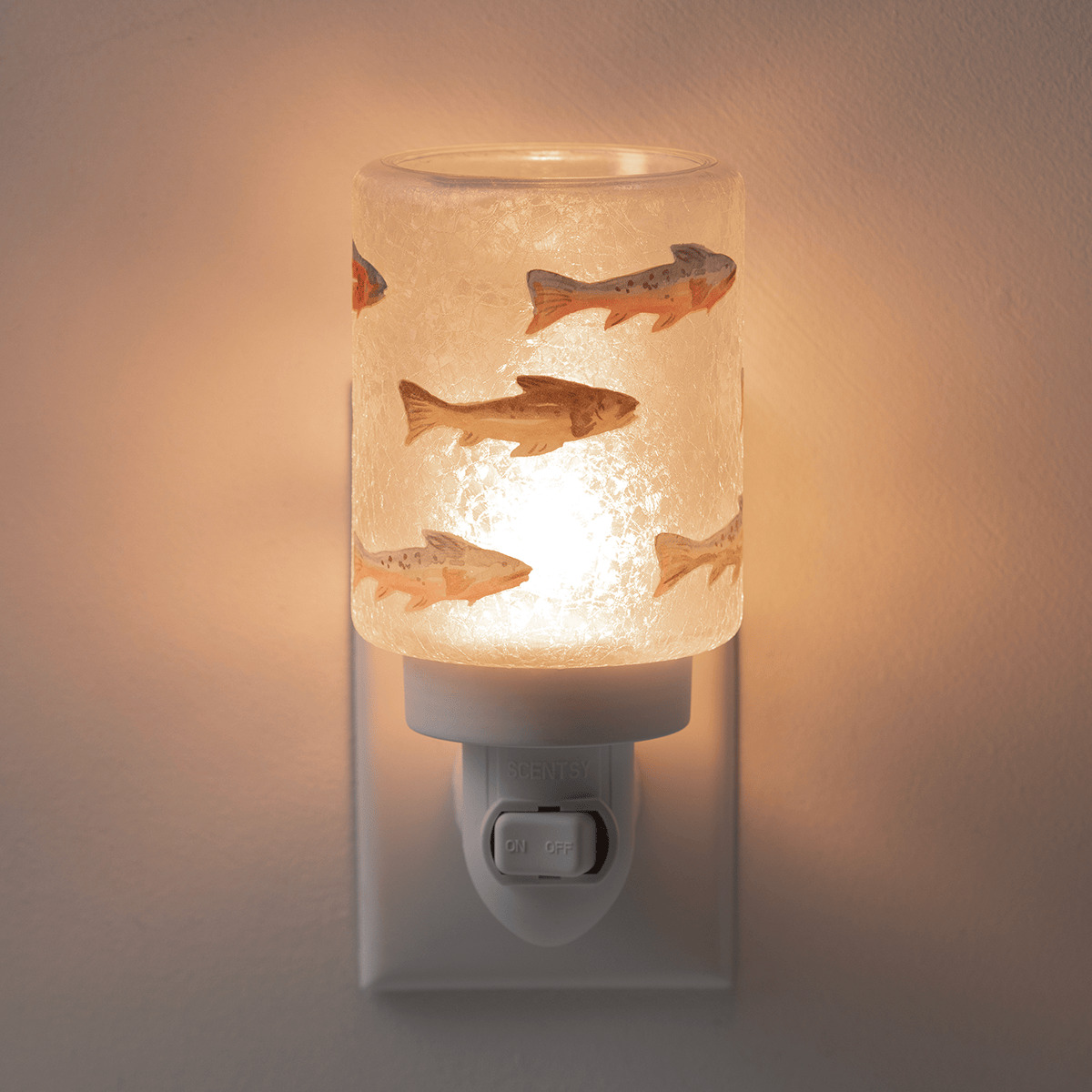 Cylindrical frosted glass mini warmer with fish silhouettes in brown and orange tones, plugged into a wall outlet and lit from within, the Silverfin Mini Scentsy Warmer