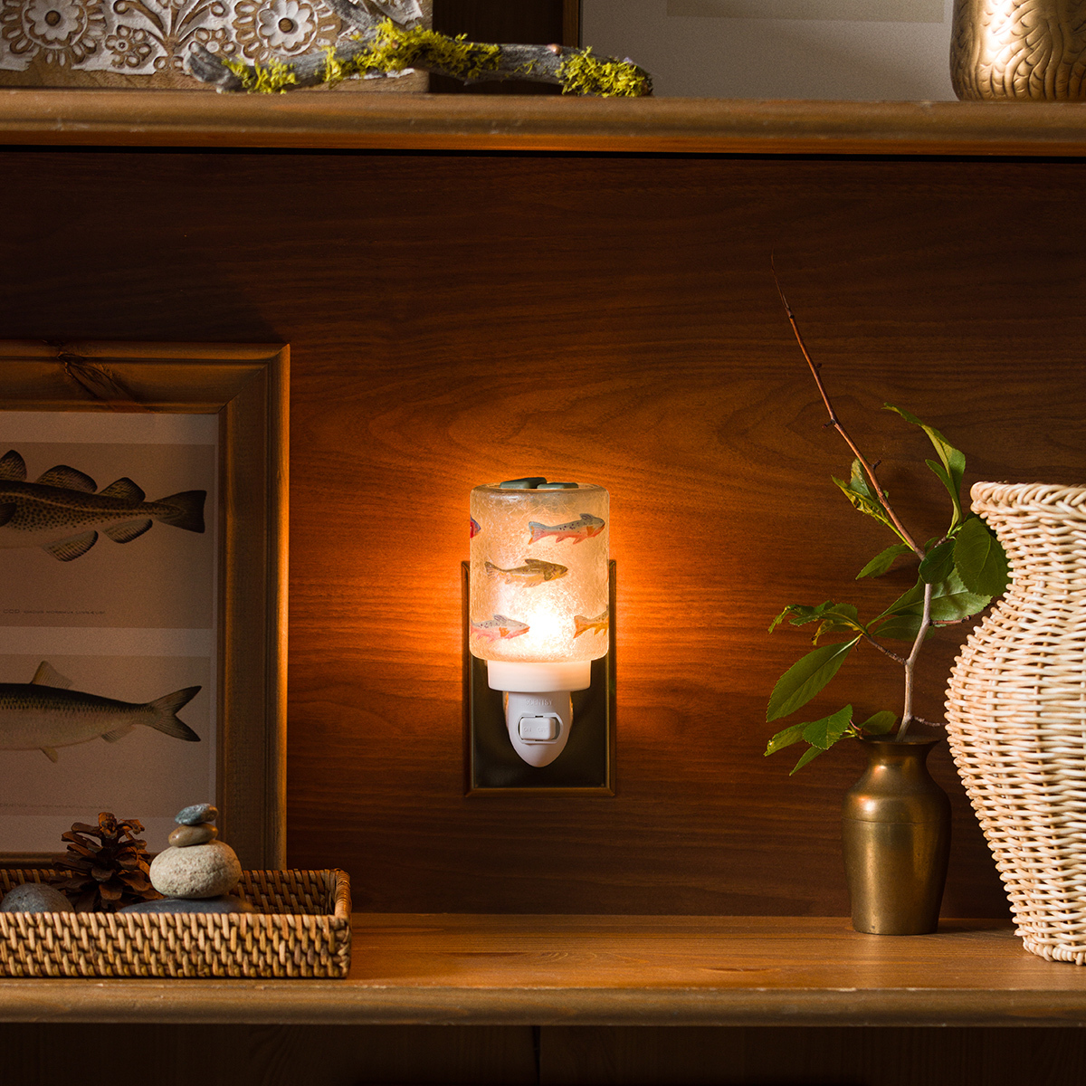 Mini warmer with an illuminated cylindrical shade featuring hand-painted goldfish and coral motifs, plugged into a wall outlet and glowing warm orange, the Silverfin Mini Scentsy Warmer