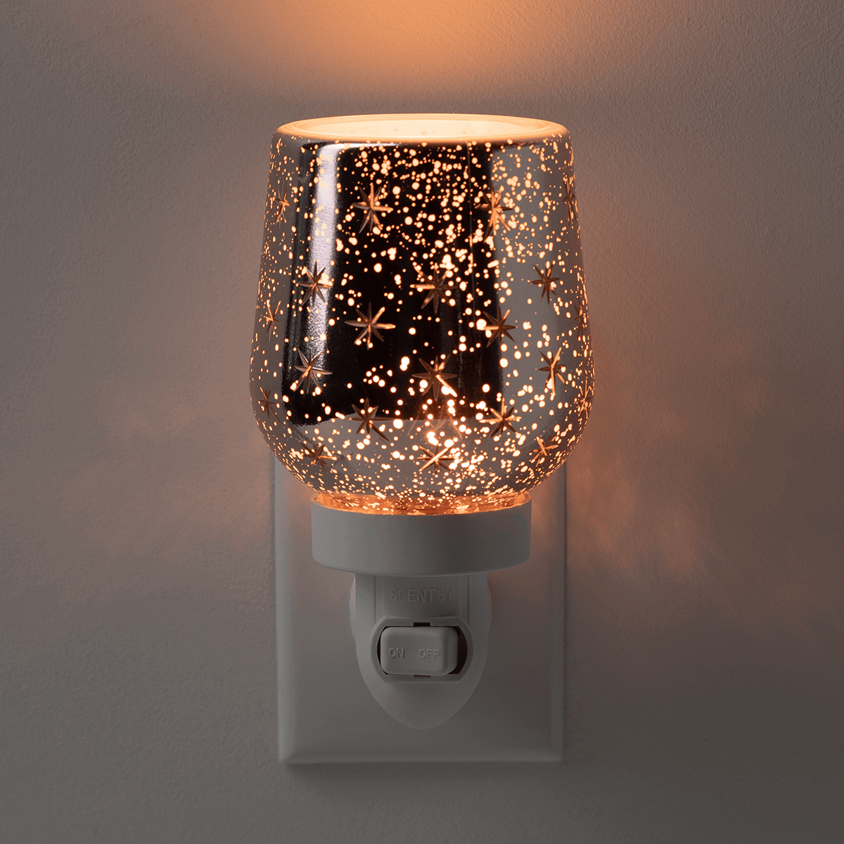 Black glass mini warmer with gold starbursts and scattered dots, glowing warm when plugged in, the Frosted Flurry design