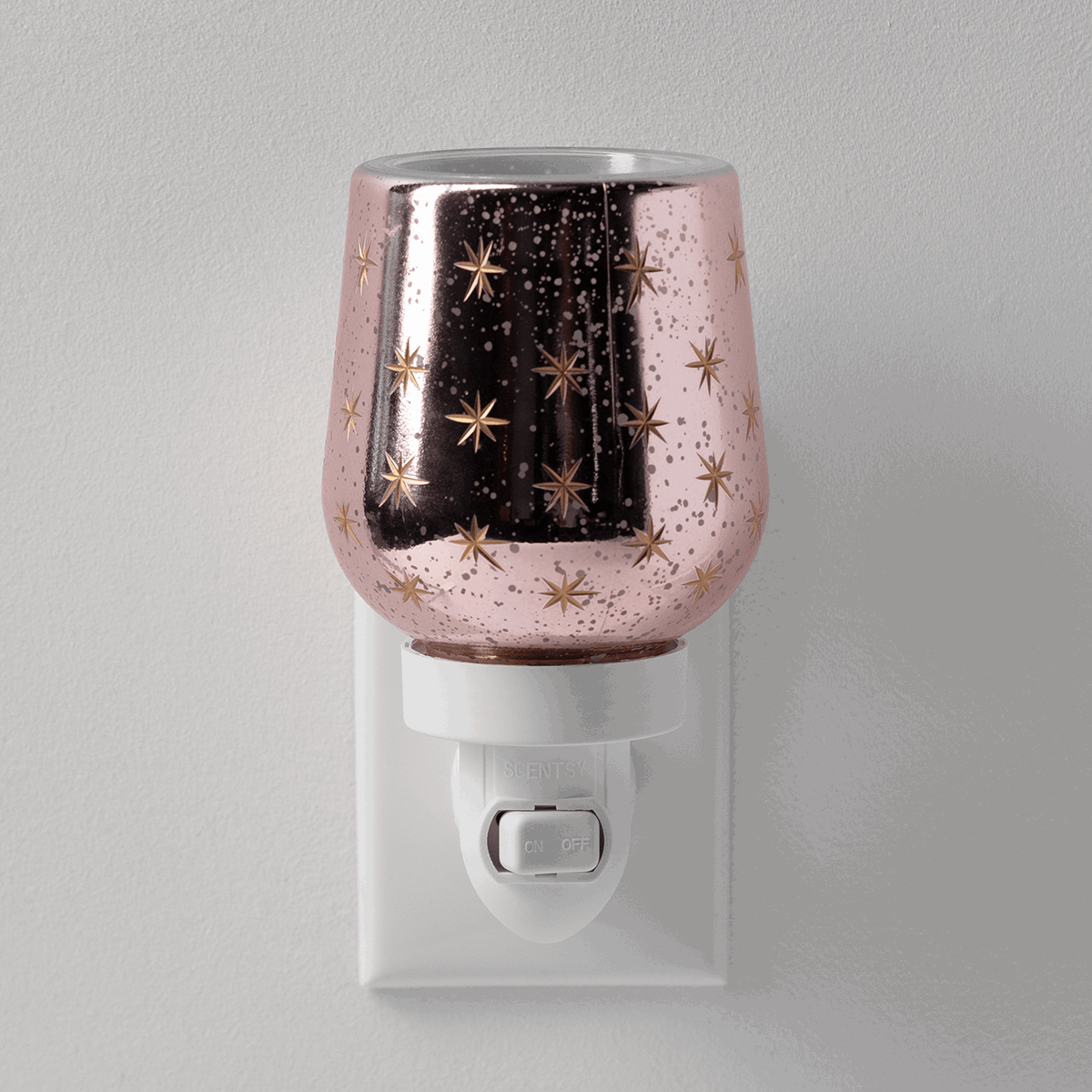 Rose-gold glittery mini warmer with gold star pattern, black vertical stripe, and white plug-in base with on/off switch, the Frosted Flurry design