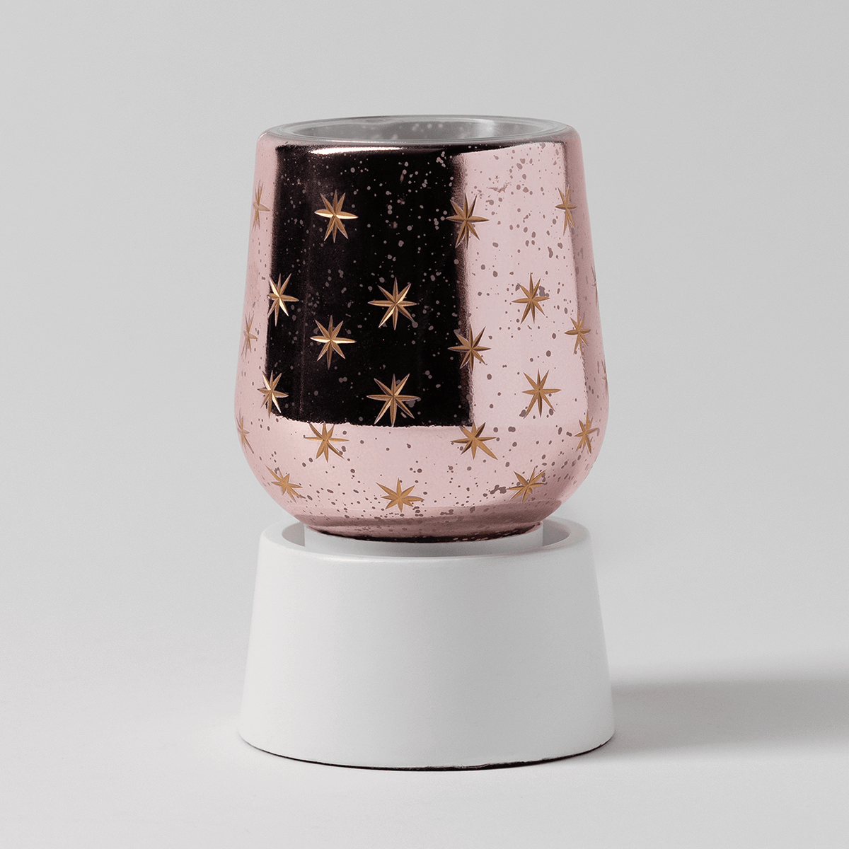 Pink speckled ceramic warmer with gold star pattern and black center panel, seated on a white cylindrical base, the Frosted Flurry Mini Scentsy Warmer