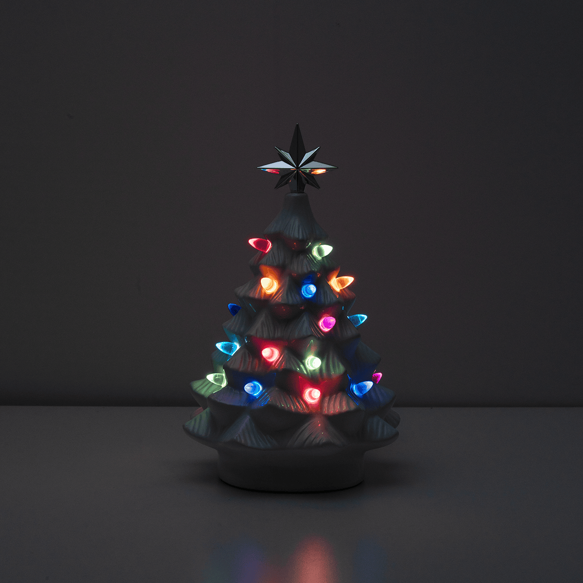 White ceramic Christmas tree warmer with illuminated multicoloured ornaments and a star topper, the Merry Little Christmas Scentsy Warmer in a dark setting