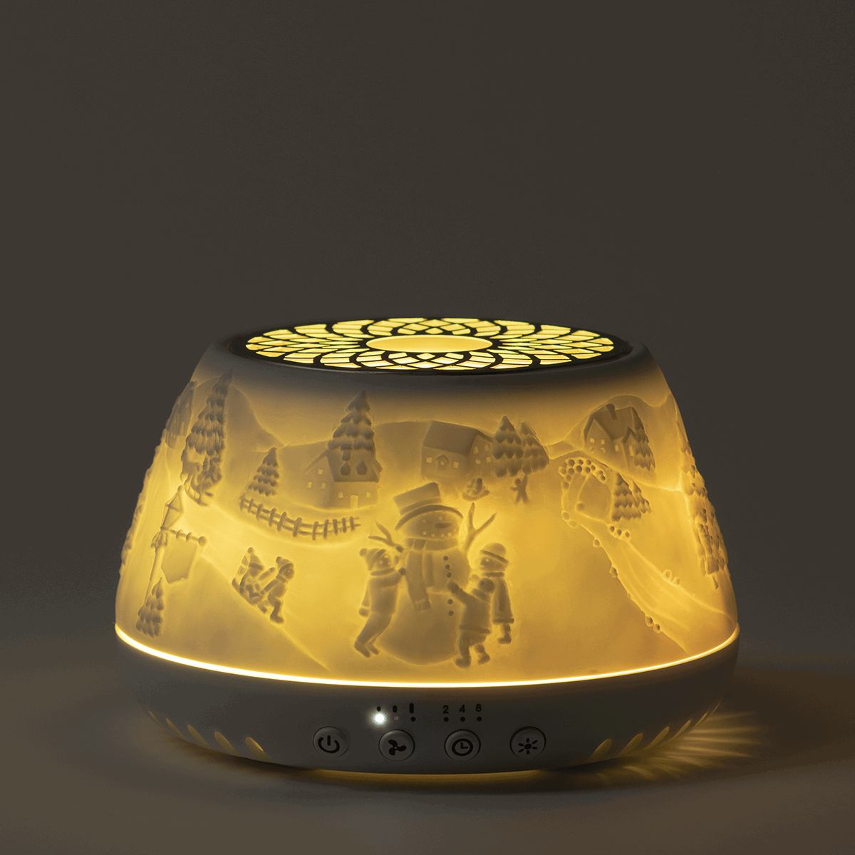 Dome-shaped Scentsy Air Quad diffuser with warm white glow, showing a winter village scene with snowman, trees, houses and children silhouetted through the translucent sides, control buttons at the base