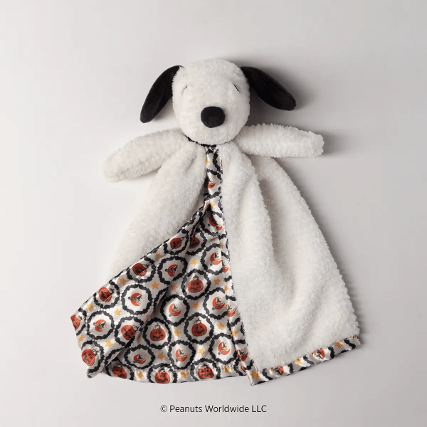 Soft white plush dog with black ears and nose wearing a patterned blanket with red pumpkins, yellow stars, and black swirls, Snoopy’s Happy Halloween Blankie Buddy