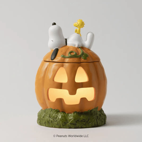 Orange carved jack-o'-lantern pumpkin with glowing cutout face on green moss base, topped with white Snoopy character and yellow Woodstock figure, the Snoopy’s Pumpkin Patch Scentsy Warmer