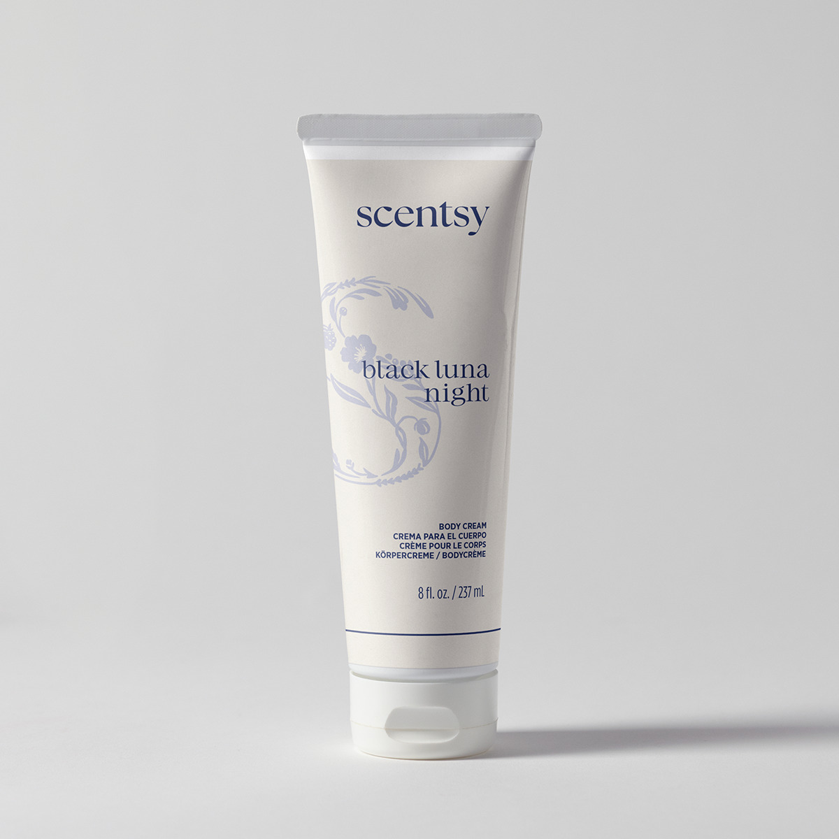 Cream squeeze tube with a flip cap and blue floral crescent artwork, the Black Luna Night Body Cream, standing on a pale grey background