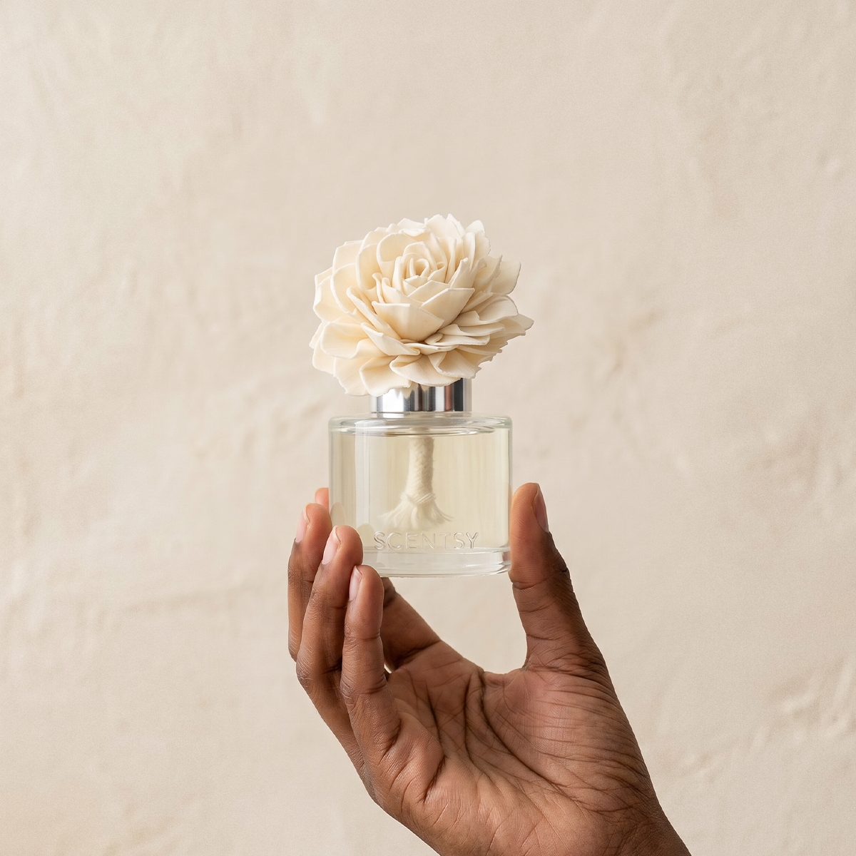 Hand holding a clear glass bottle with a silver cap topped by a cream-coloured rose, the Blackberry Dahlia Dahlia Darling Fragrance Flower