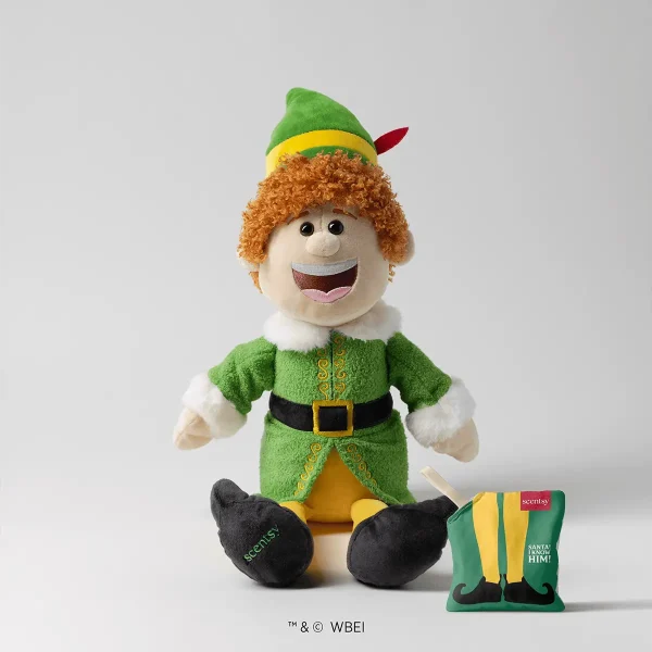 Buddy the Elf Scentsy Buddy plush toy with curly orange hair, bright smile, green elf outfit with yellow trim, black belt, white fur collar and cuffs, black shoes, alongside festive green and yellow packaging
