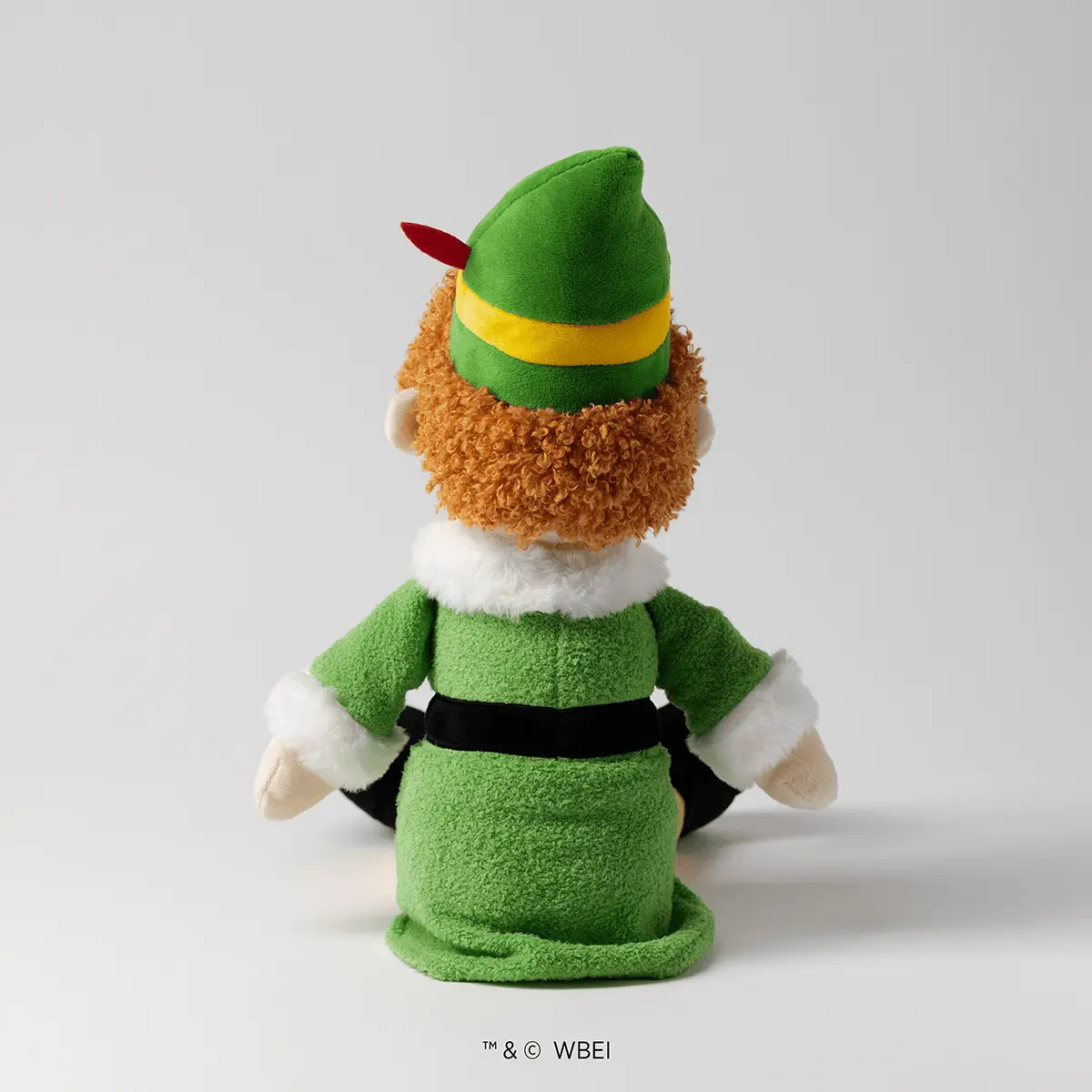 Soft plush character with a tan curly-haired head, green pointed hat with a yellow band and red feather, bright green fleece body with white fur collar and cuffs, and black belt detail