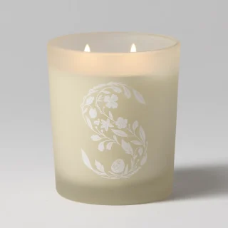 Cream-coloured pillar candle with two lit wicks and an embossed white floral and leafy wreath design, the Christmas Cottage Scentsy Candle