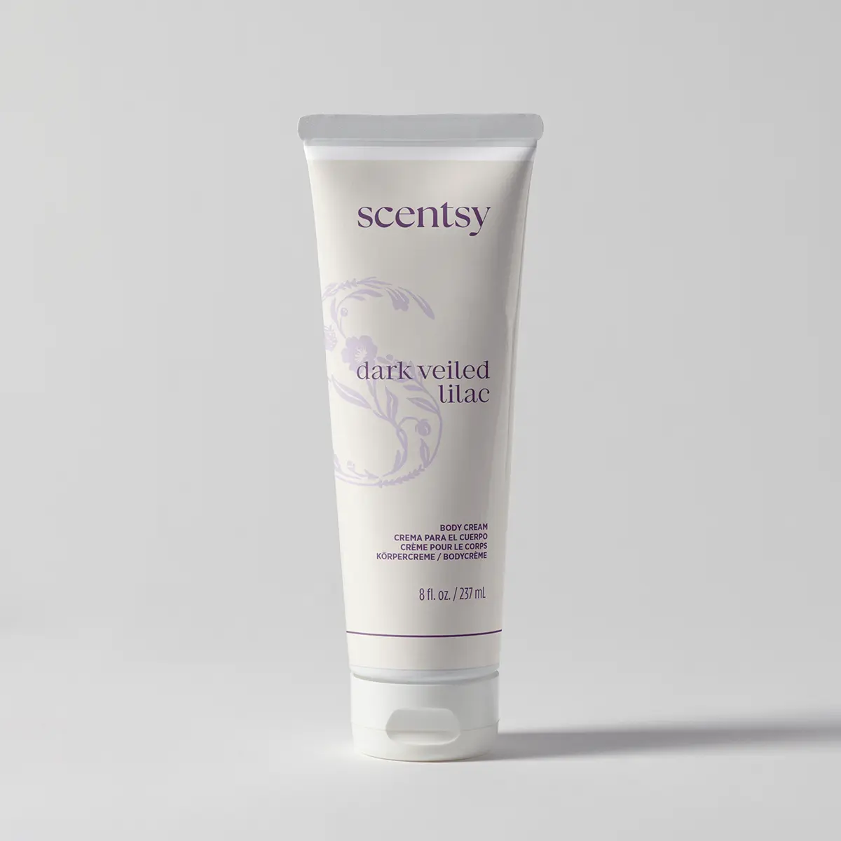 Cream squeeze tube with a flip cap and purple floral scrollwork, holding Dark Veiled Lilac Body Cream, shown upright against a soft grey backdrop