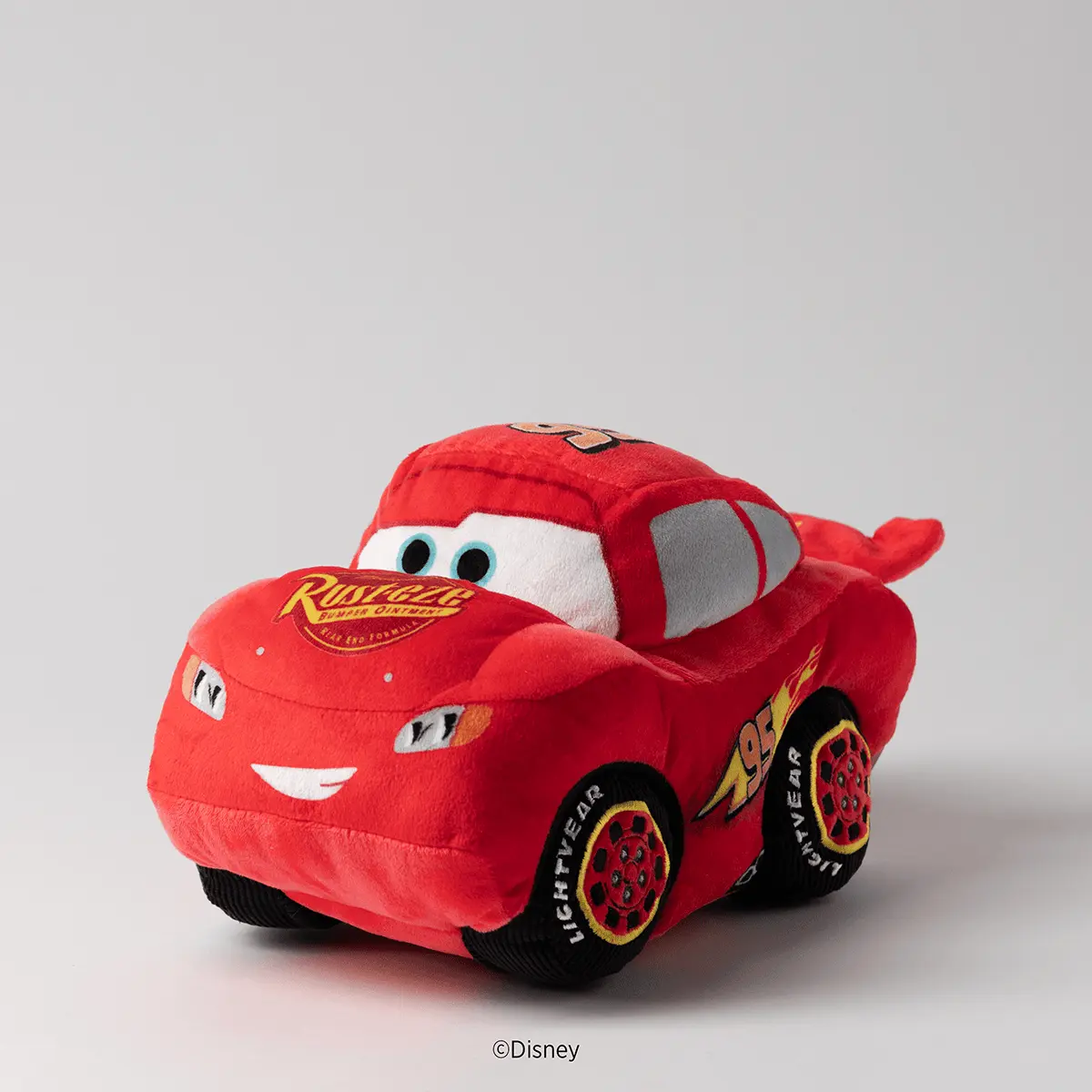 Red plush toy car with a smiling face, white eyes, and black tyres, featuring the Radiator Springs logo and "Lightyear" text on its side