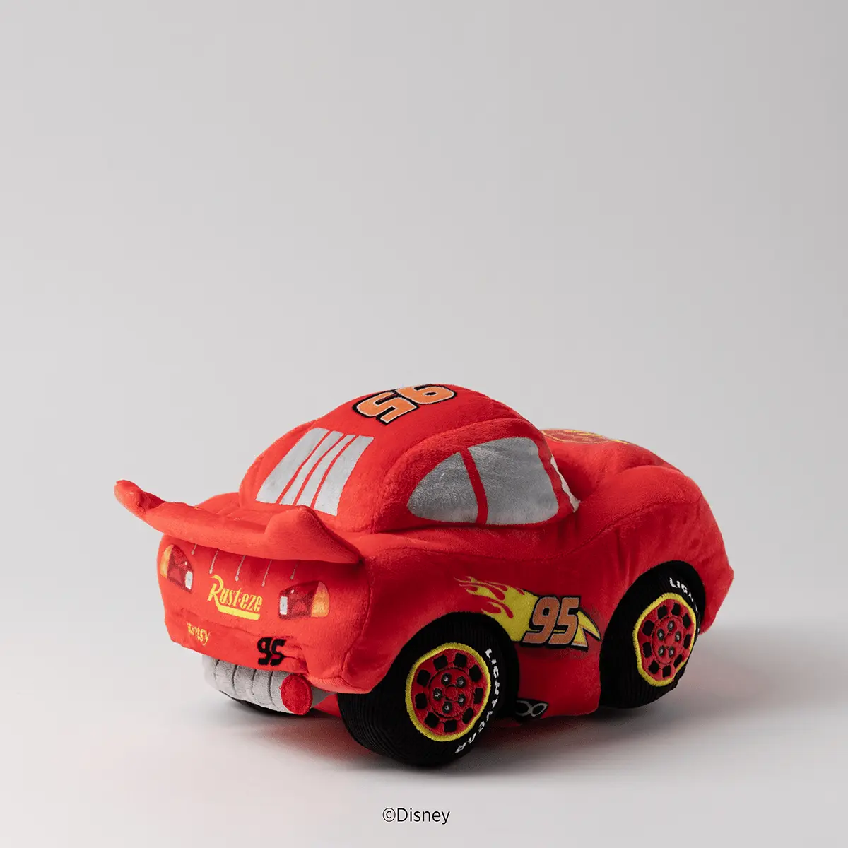 Red plush racing car toy with number 95, yellow flame design, grey racing stripe, and black wheels with red details