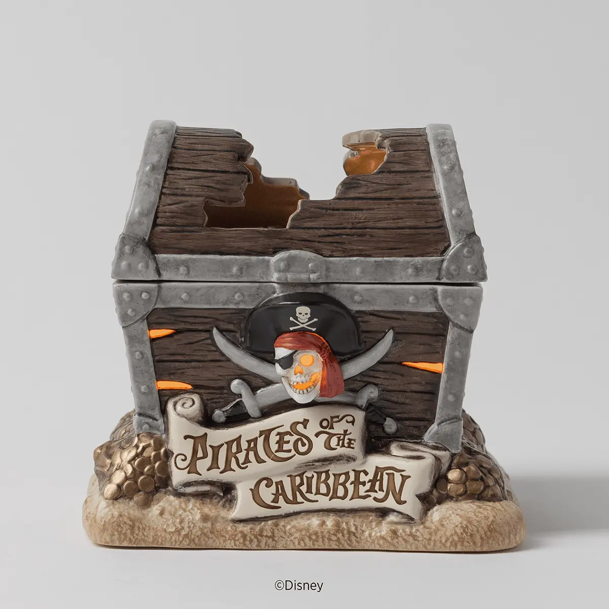 Decorative wooden treasure chest with grey metal corners and a skull-and-crossbones pirate design on the front, sitting on a sand-textured base, the Disney Pirates of the Caribbean Scentsy Warmer