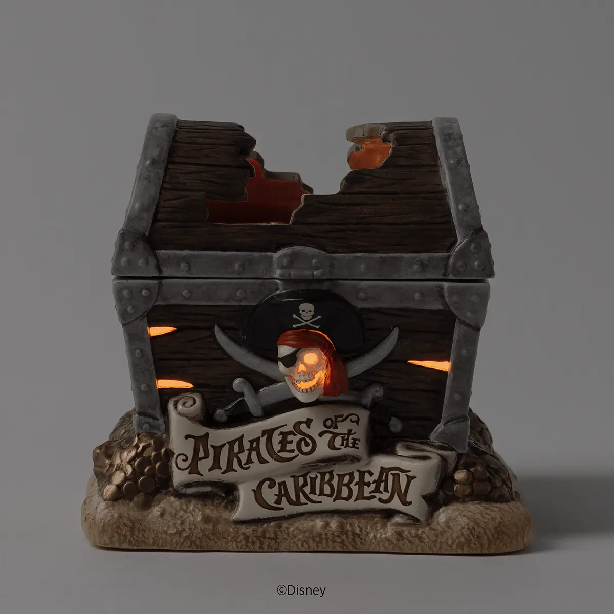 Pirate-themed Scentsy Warmer with a grey metal-banded treasure chest, glowing skull and crossbones emblem, illuminated side vents, and sandy base, the Disney Pirates of the Caribbean Scentsy Warmer