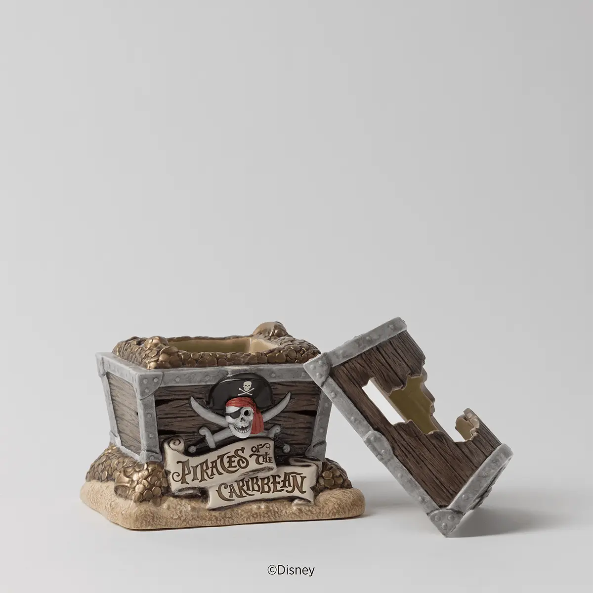 Decorative warmer shaped like a wooden treasure chest with skull and crossbones emblem, removable hinged lid, and sand base, accompanied by a separate wooden plank-styled dish