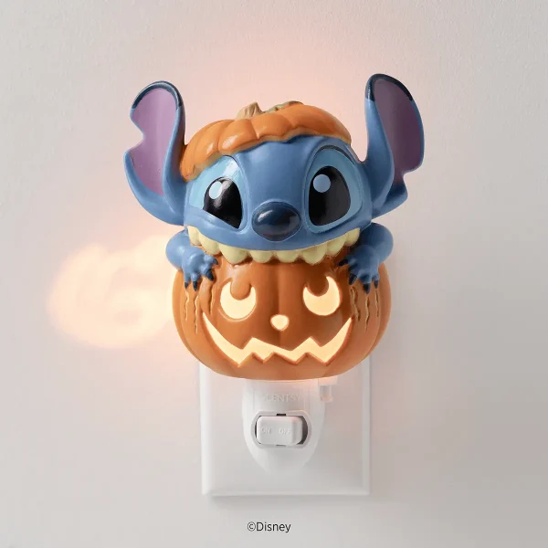Blue alien character with large ears and orange pumpkin head sitting atop an orange jack-o'-lantern with glowing carved face, mounted on a white wall plug, the Disney Stitch: Pumpkin Trouble Mini Scentsy Warmer