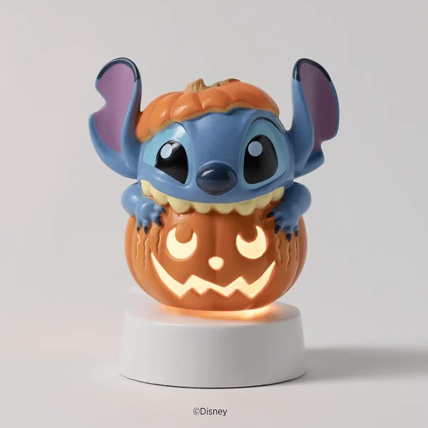 Blue character with large ears and orange pumpkin head sitting atop a carved jack-o'-lantern with illuminated face on white base, the Disney Stitch: Pumpkin Trouble Mini Scentsy Warmer with Tabletop Base