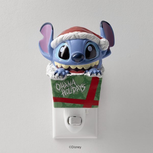 Blue alien character with large ears wearing a red and white Santa hat, sitting in a green gift box with red ribbon and "Ohana Holidays" text, mounted on a white Scentsy wall plug, the Disney Stitch: Unleash the Holidays Mini Scentsy Warmer