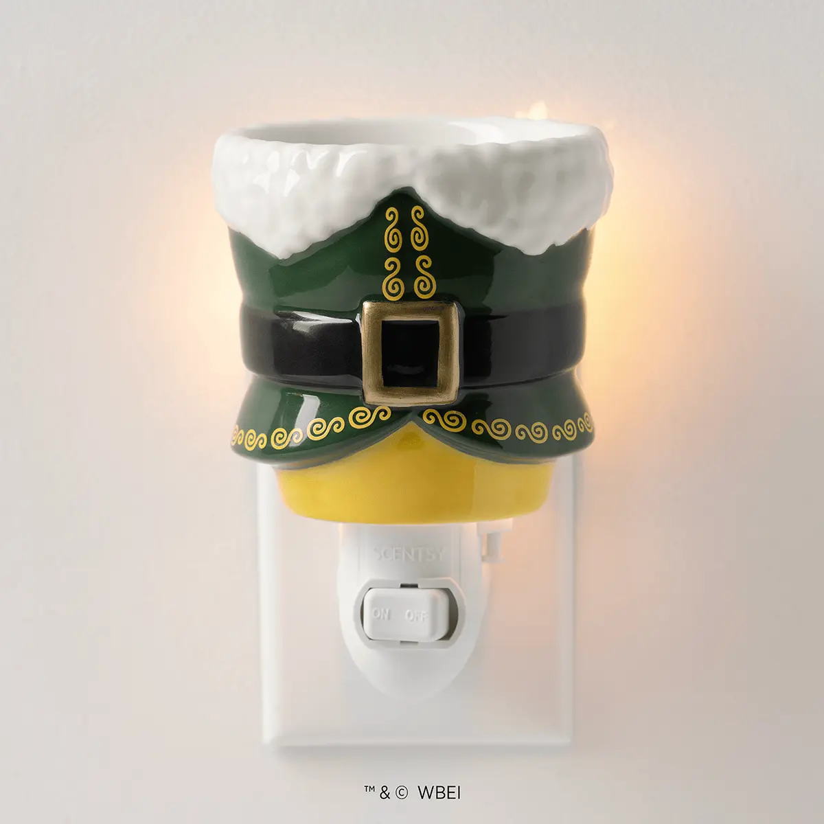 White plug-in warmer topped with a decorative elf hat in green and black with white fur trim, gold scroll details, and a buckled belt, featuring a yellow wax reservoir, the Elf: Buddy's Christmas Joy Mini Scentsy Warmer