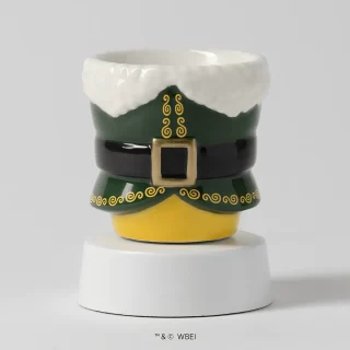 Green ceramic mini warmer shaped like Buddy the Elf's suit with a white collar and black belt, on a white tabletop base