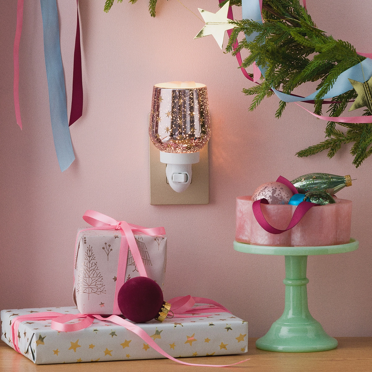 Frosted Flurry Mini Scentsy Warmer with rose-gold glitter upper globe and white plug base, displayed in a festive holiday scene with wrapped gifts, evergreen garland, and ornaments