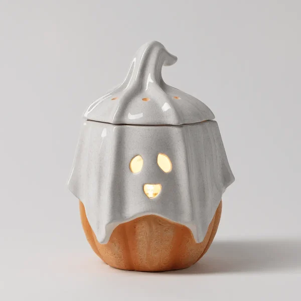 Ceramic warmer shaped like a pumpkin with a ghost draped over it, the upper half glossy white with a spooky face cutout glowing warm, lower half terracotta orange, topped with a dog-shaped finial, the Ghostlight Gourd Scentsy Warmer