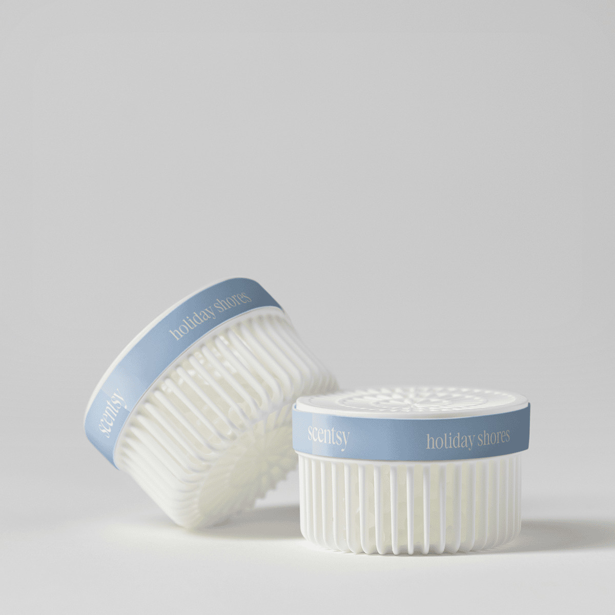 Two white ridged Scentsy Pods with blue and white bands labelled "Scentsy" and "holiday shores," one upright and one tilted