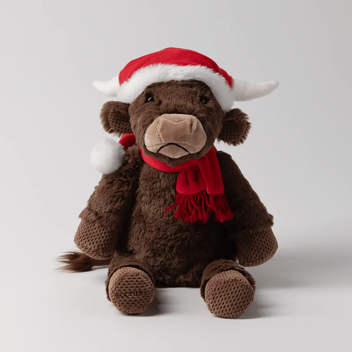Brown plush cow with a tan snout and floppy ears, wearing a red Santa hat with white trim, red scarf, and tan knitted sweater, the Jolly Ol' Saint Moo Scentsy Buddy