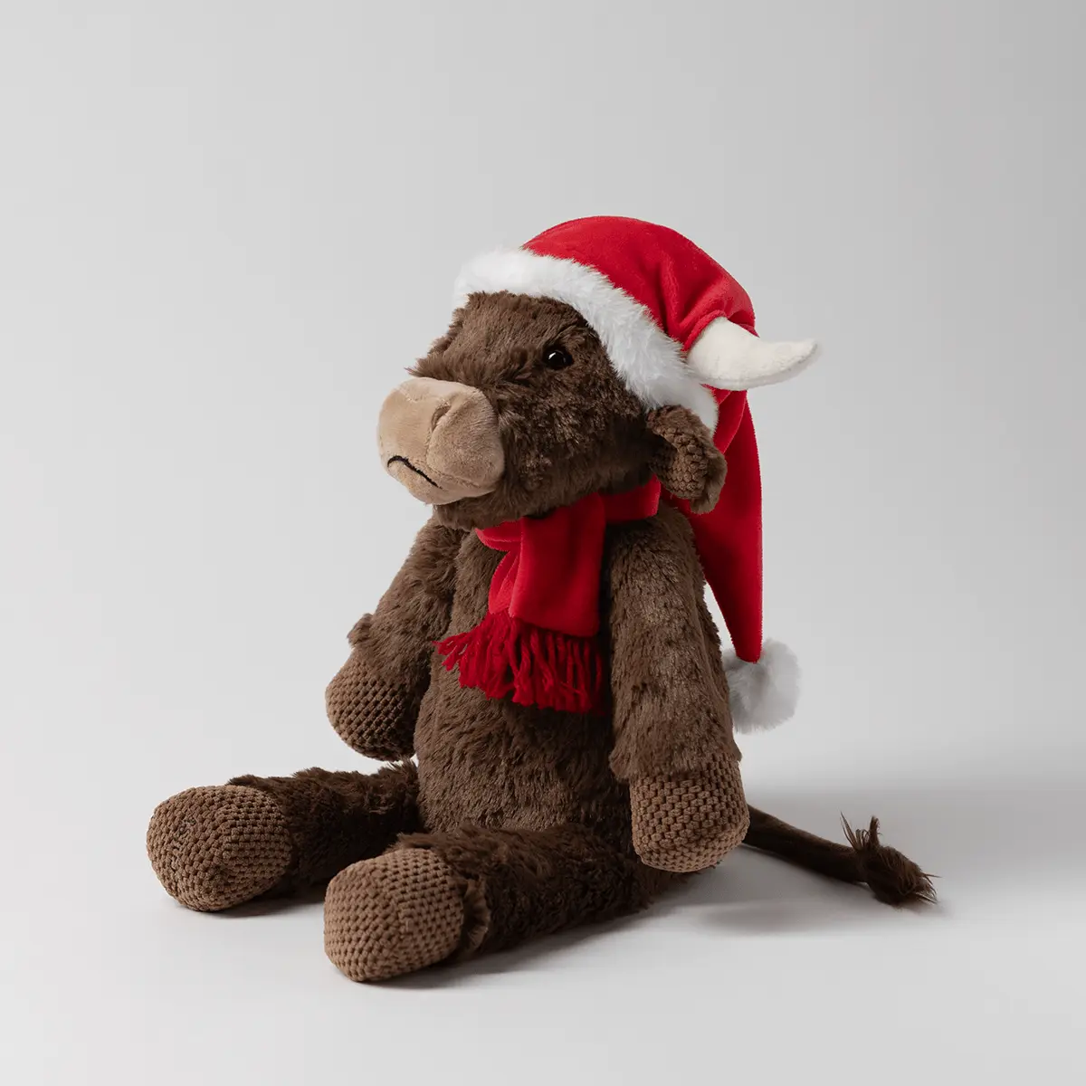 Brown plush moose with textured knit limbs and tail, wearing a red Santa hat with white trim and a red scarf