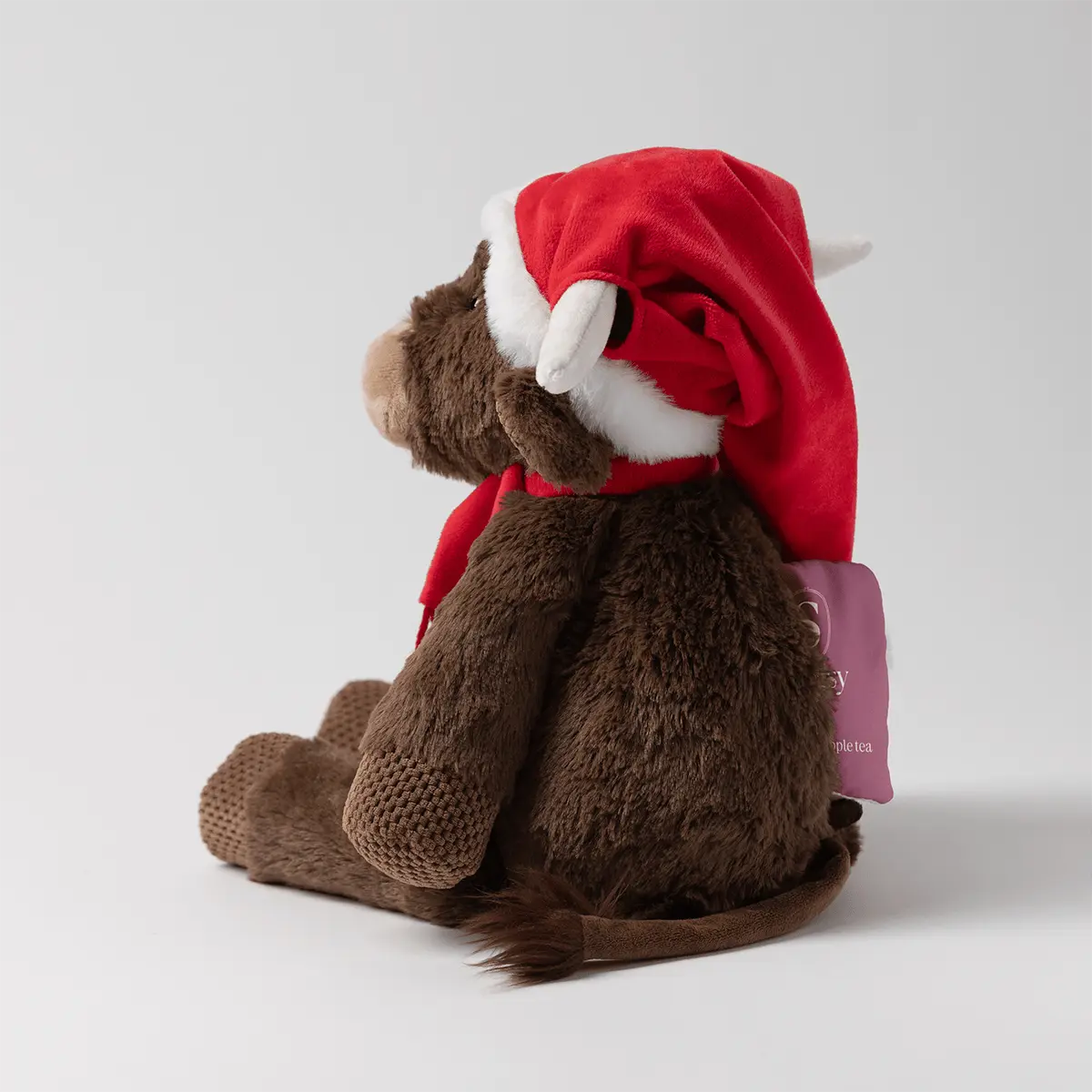 Brown plush cow wearing a red Santa hat with white trim and a red scarf, with cream-coloured horns and a textured tan snout