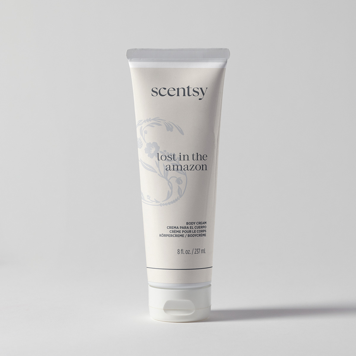 Cream-coloured squeeze tube with a white flip cap and soft blue floral line art, the Lost in the Amazon Body Cream, standing upright against a pale grey background