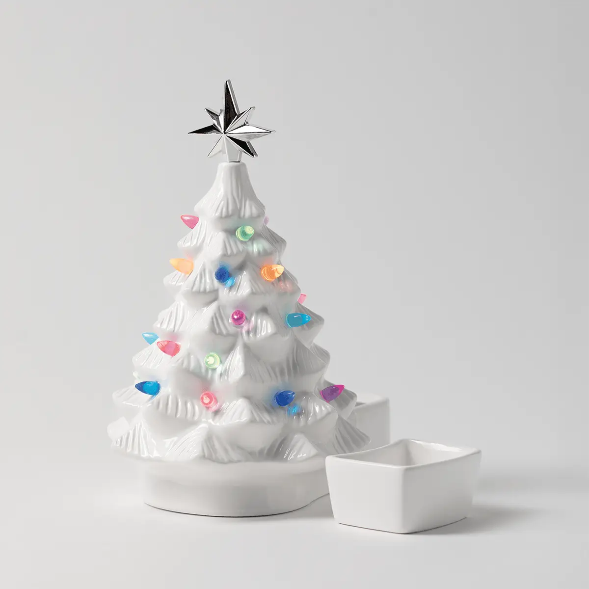 White ceramic Christmas tree warmer with textured branches, topped by a silver star and decorated with colourful gemstone accents, accompanied by a white dish, the Merry Little Christmas - White Scentsy Warmer