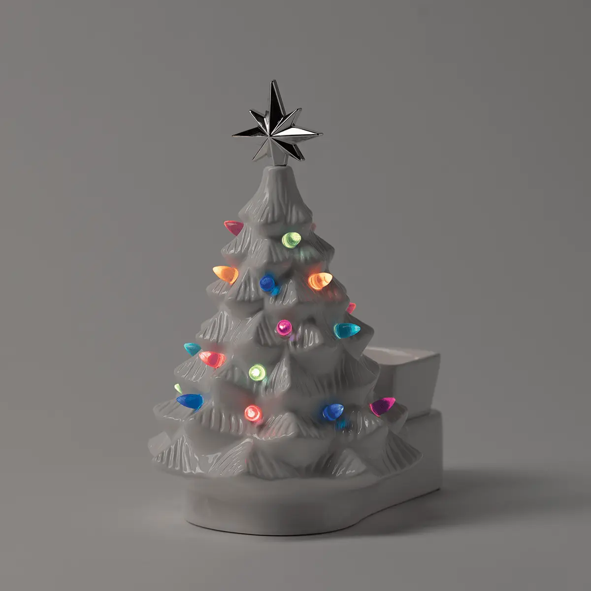 White ceramic Christmas tree warmer with textured branches, topped with a dimensional metal star, and adorned with colourful illuminated ornaments in red, pink, blue, orange, green and teal