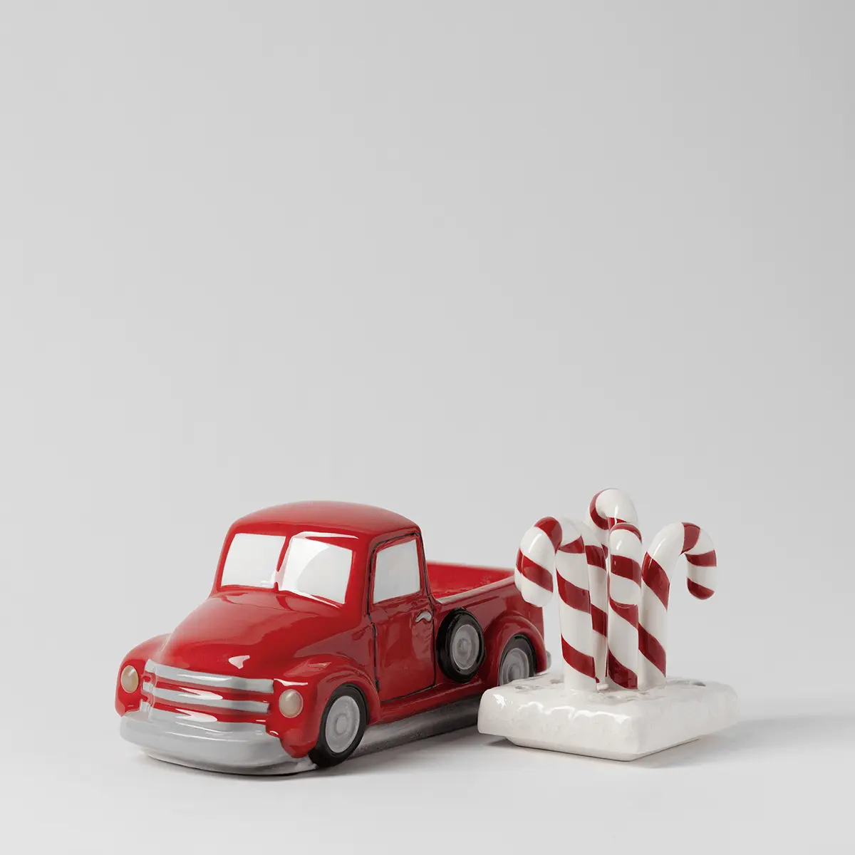 Red ceramic retro truck warmer with white-wall tyres, paired with a white base holding three red-and-white striped candy cane toppers