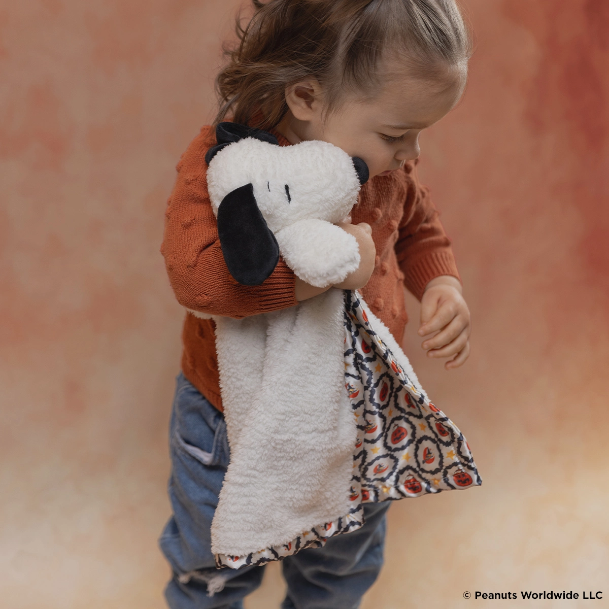 Soft plush dog toy with white and black face, orange ears, and an attached patterned fabric blanket section in autumn colours
