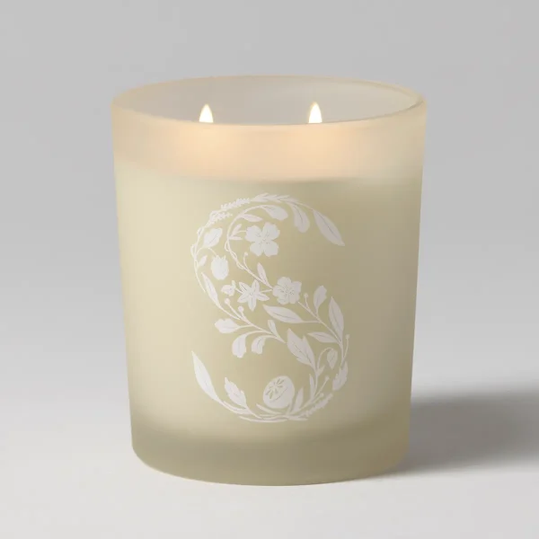 Cream-coloured candle with two lit wicks and an ornate white floral and leaf pattern etched across the front, the Snowberry Scentsy Candle