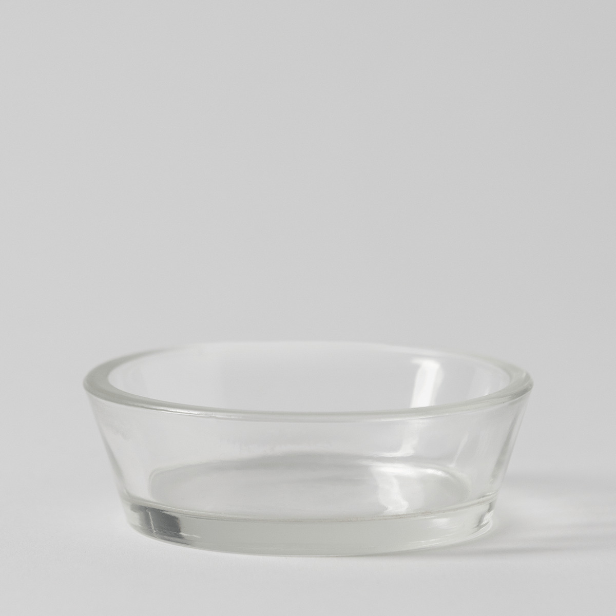 Clear shallow round glass dish with tapered sides and a thick rim on a pale grey background, the Boo's Treats Replacement Dish