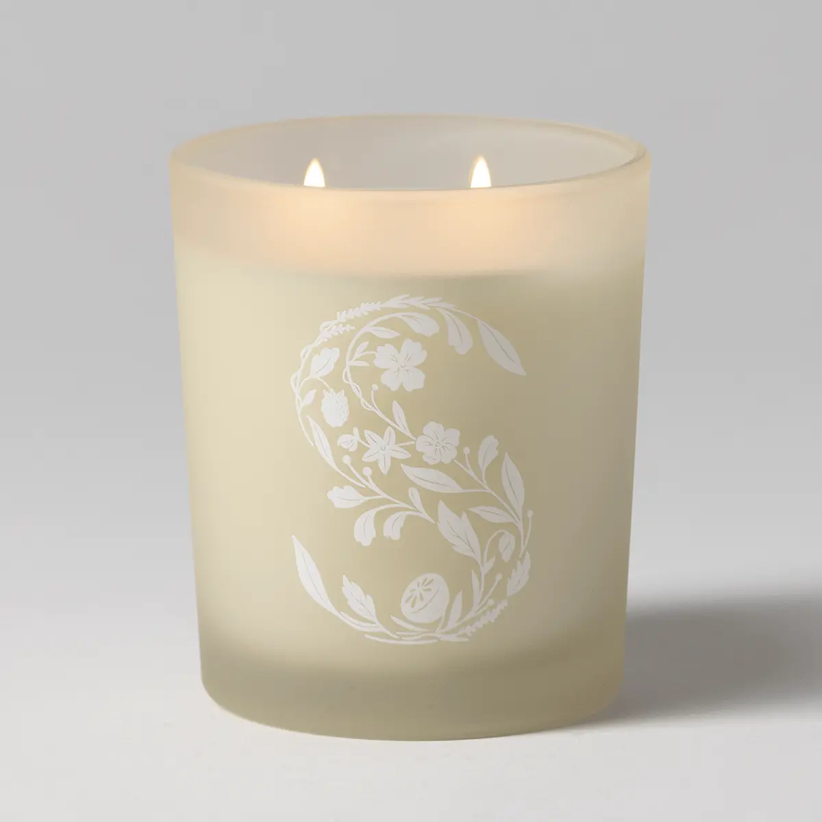 Cream-coloured pillar candle with two lit wicks and an embossed white floral and leafy wreath design, the Christmas Cottage Scentsy Candle