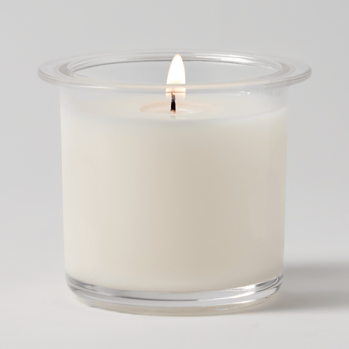 Cream wax candle in clear glass vessel with flared rim and lit cotton wick, the Cocoa Cashmere Candle Insert