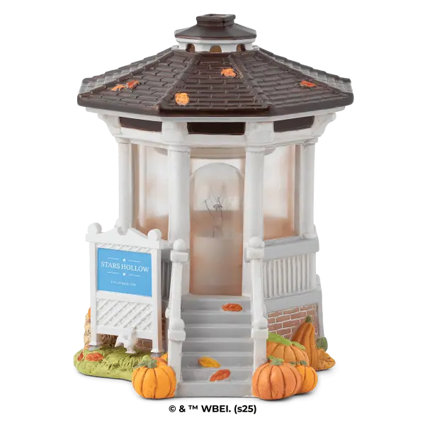 White gazebo-style warmer with a grey shingled roof and amber accent lights, surrounded by decorative pumpkins and autumn leaves, the Gilmore Girls: Welcome to Stars Hollow Scentsy Warmer