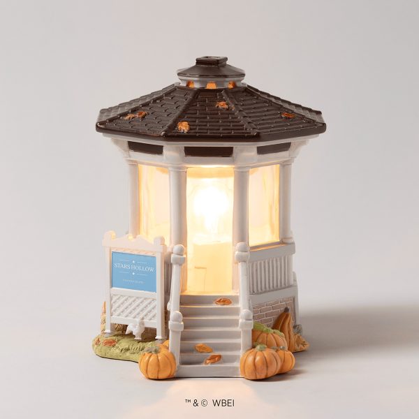 Miniature gazebo-style warmer with cream pillars and dark roof, lit from within with warm glow, surrounded by decorative pumpkins and autumn leaves with a Stars Hollow sign, the Gilmore Girls: Welcome to Stars Hollow Scentsy Warmer