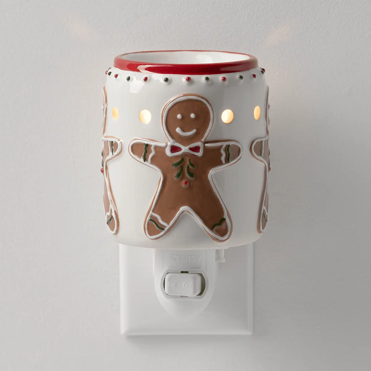 White ceramic plug-in warmer with a red rim and smiling gingerbread men in bow ties, lit from within, the Gingerbread Snap Mini Scentsy Warmer