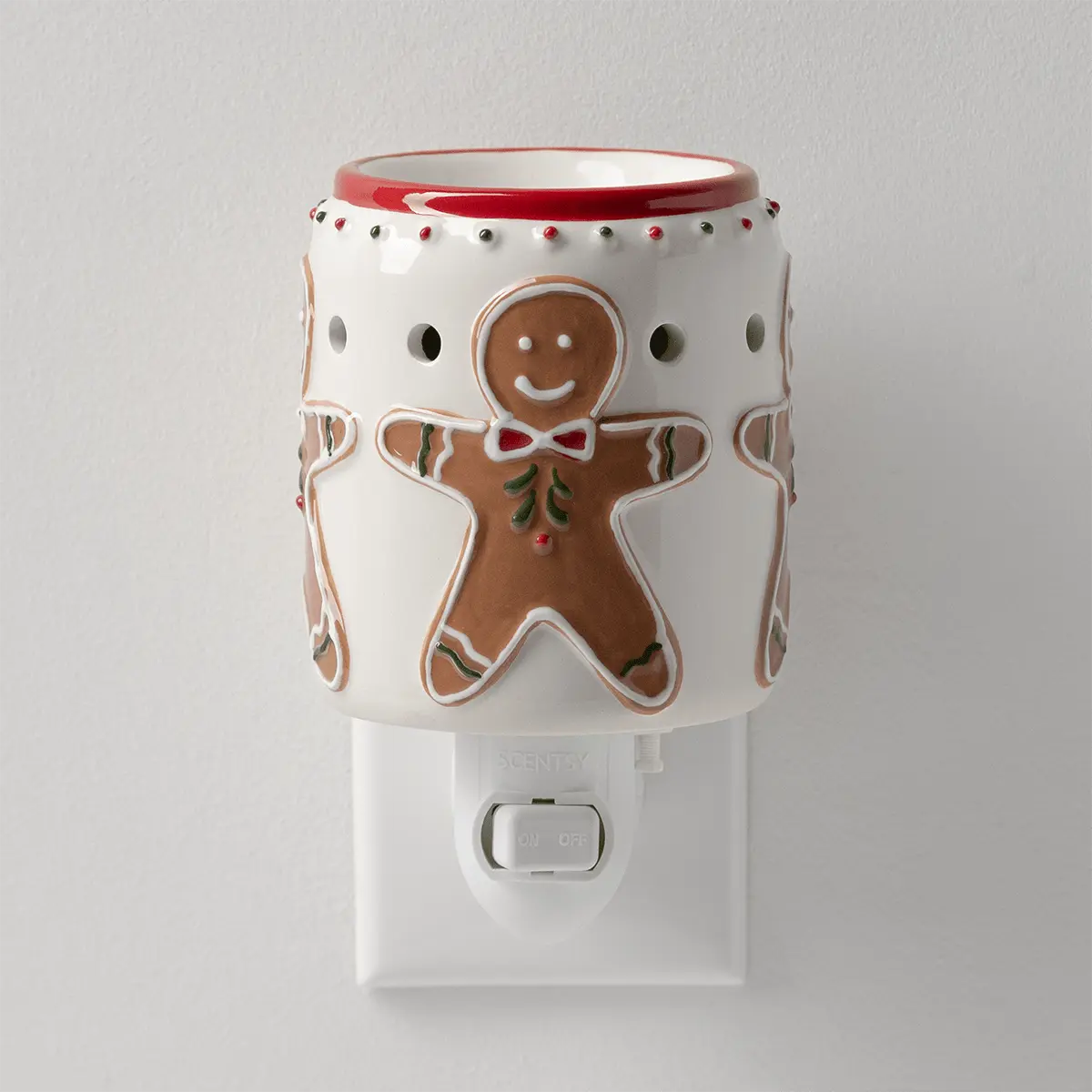 White ceramic plug-in mini warmer with a red rim, raised gingerbread men in red bow ties and red and green dots, on a wall socket