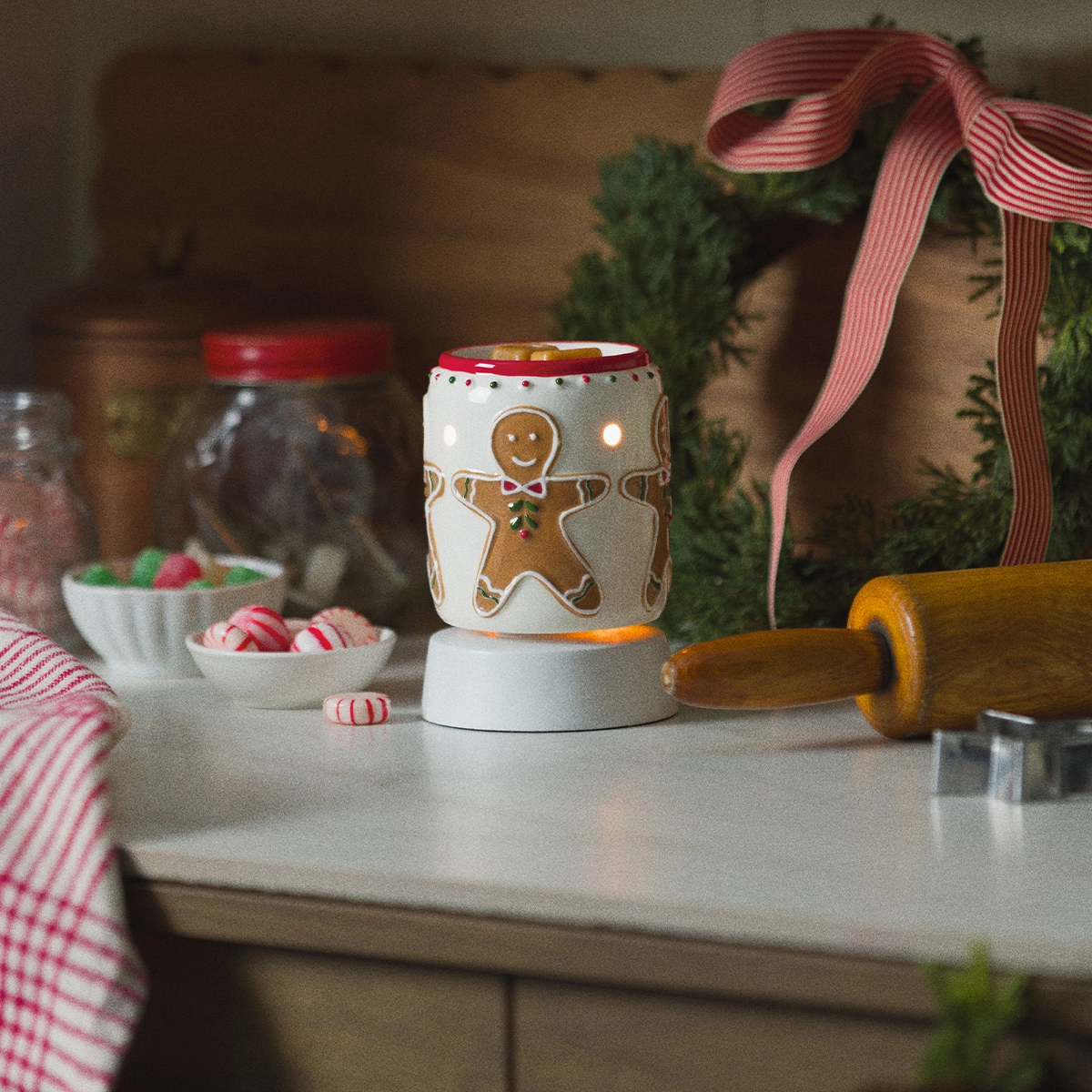 Mini Scentsy Warmer with gingerbread man design in cream and brown, topped with a red and gold lid, displayed on a white tabletop base in a festive kitchen setting