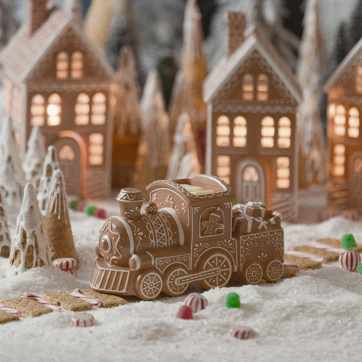 Gingerbread-style ceramic train warmer with white icing details and a wax dish in the cab, set in a snowy gingerbread village