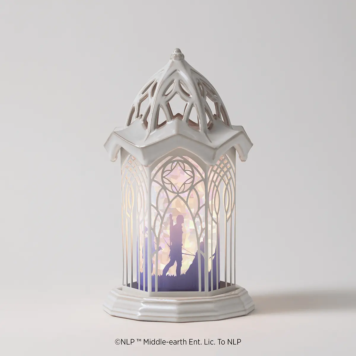 White ceramic warmer with a pointed spire roof and geometric cutout patterns, featuring an illuminated scene of a silhouetted archer figure in an archway with gradient lighting from warm to cool tones, the Lord Of The Rings: Rivendell Scentsy Warmer